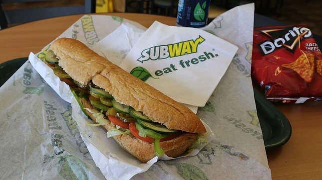 Subway footlong sandwich, bag of Doritos, and a bottle of water on Subway tabletop